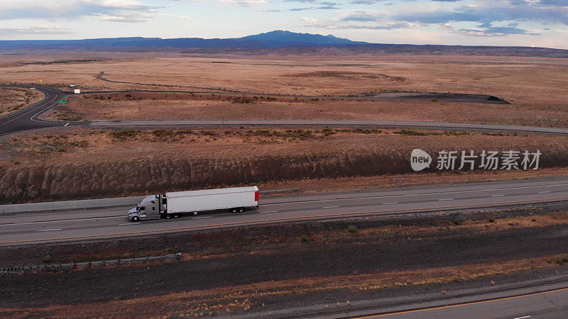 Long Haul Freight Hauler Semi-Truck and Trailer Traveling on a Four-Lane Highway in a desolate desert at dusk or dawn